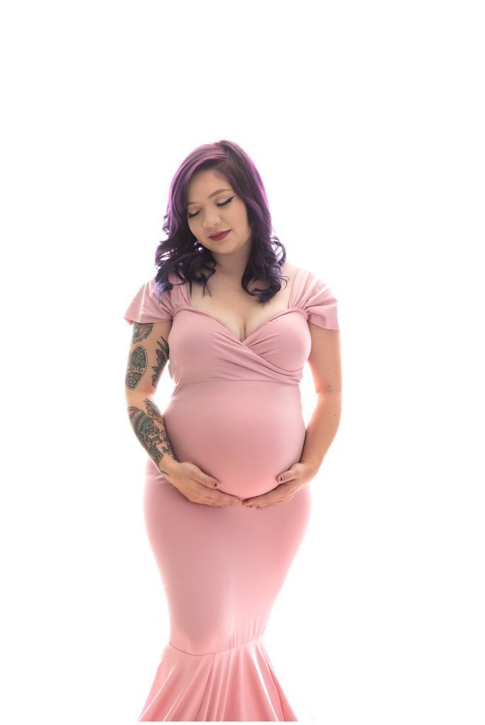 Pregnant mom in a pink gown, in front of a white backdrop.