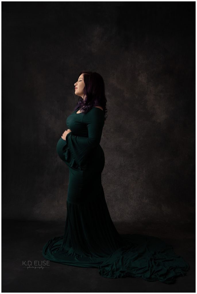 In studio maternity photography photo of pregnant mom in a dark green gown.