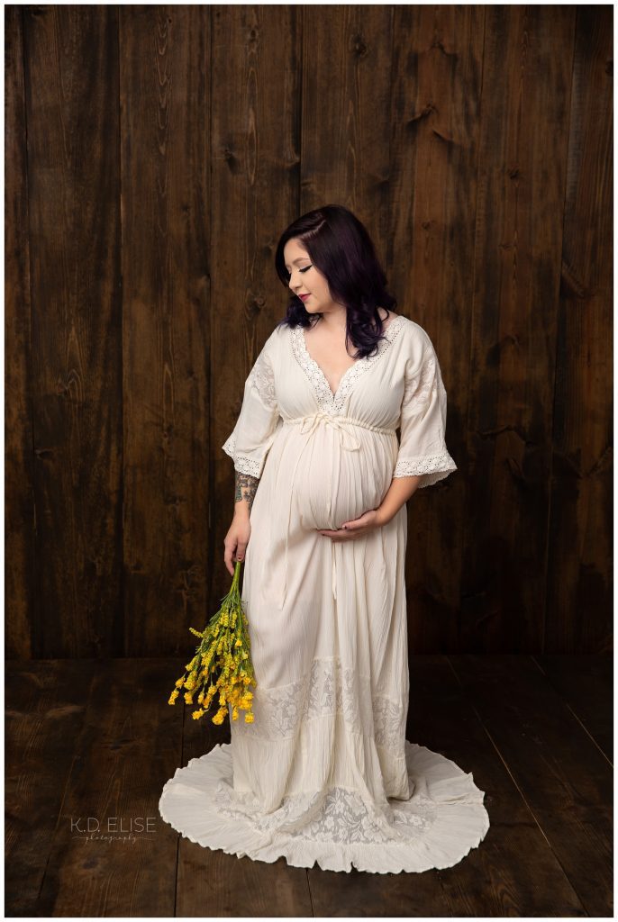 In studio maternity photography portrait of pregnant mom in a cream gown, holding a bouquet of wildflowers.