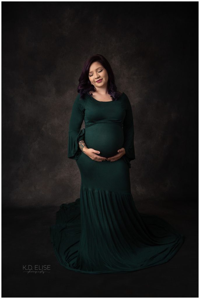 In studio maternity photography portrait of pregnant mom in a dark green gown.