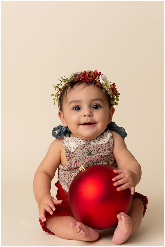 Baby girl holding a red Christmas ornament during milestone session.