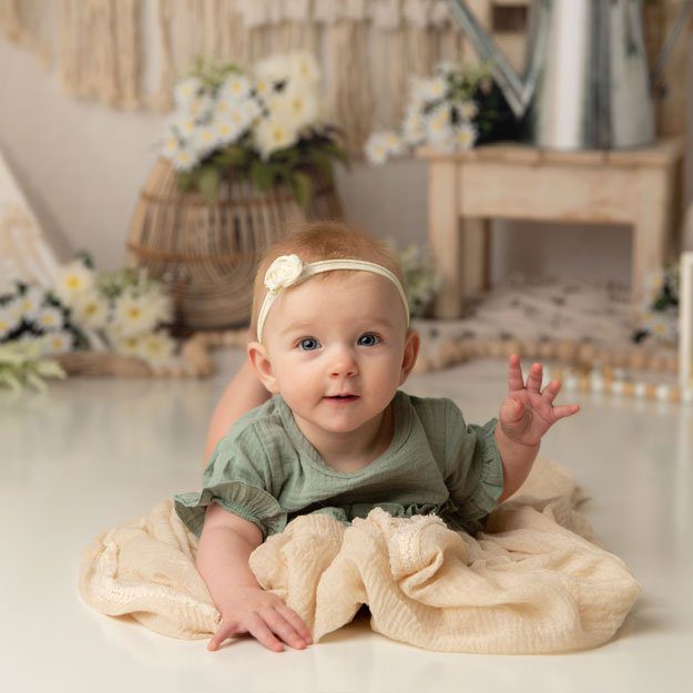 Baby girl in green outfit in front of boho themed backdrop. Milestone photo by K.D. Elise Photography.